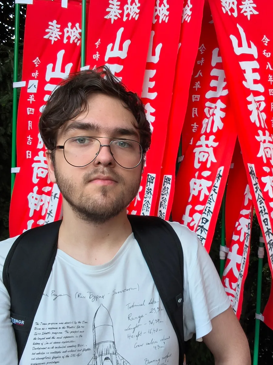 Ksawery in front of red Sanno banners at Hie Shrine in Tokyo, wearing a backpack